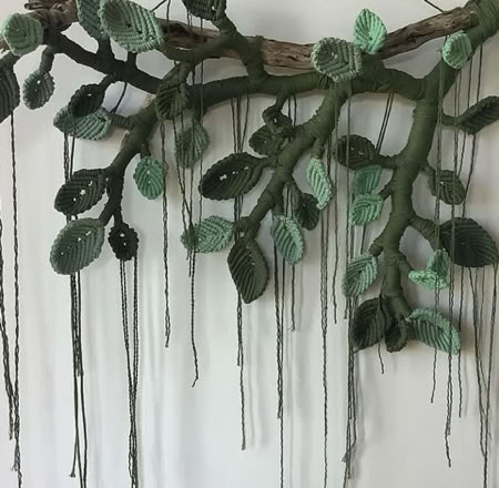 A wall-mounted art piece resembling a tree branch with green leaves and long, hanging strands.