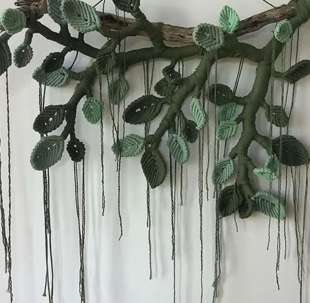 A wall-mounted art piece resembling a tree branch with green leaves and long, hanging strands.
